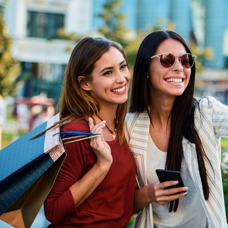 Two women smiling with shopping bags outside.