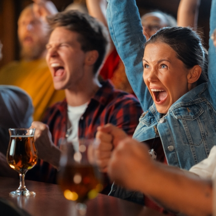 Excited fans cheering with drinks in a bar.