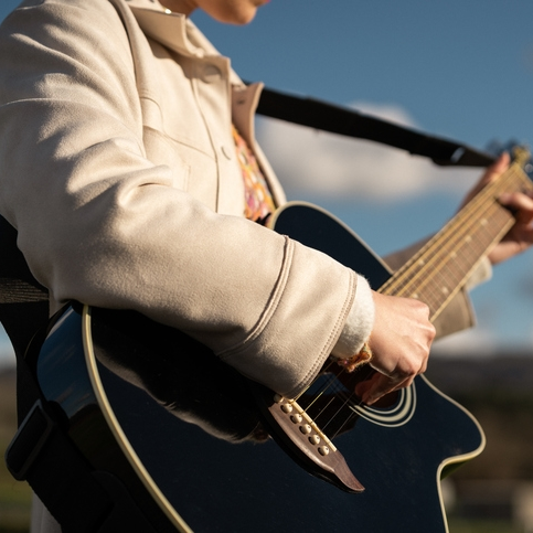 Person playing a black acoustic guitar outdoors.