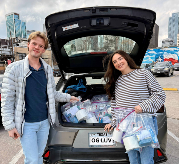 Two people with donation bags by car trunk.
