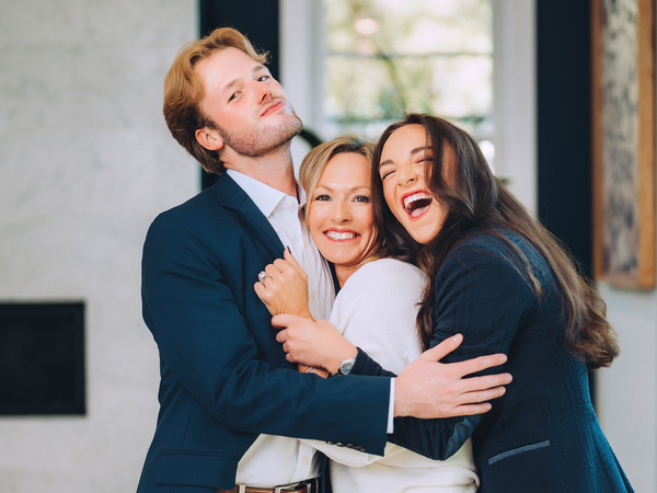 Three people hugging and smiling indoors