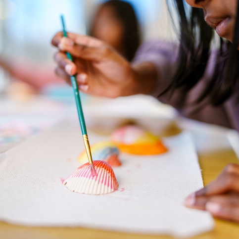 Child painting seashell with small brush