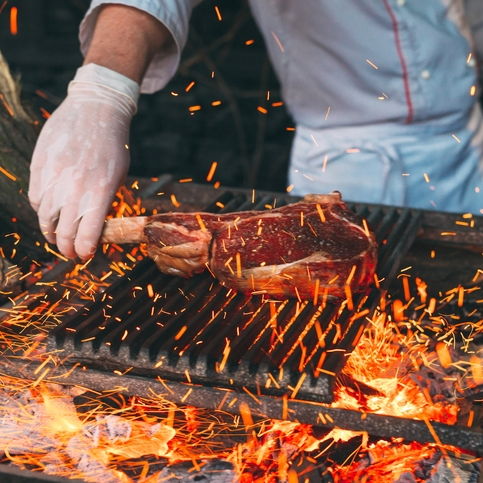 Chef grilling tomahawk steak over open flames