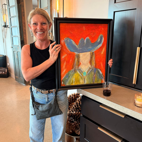 Woman holds framed colorful cowboy portrait in kitchen