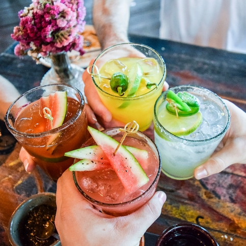 Four colorful cocktails with fruit garnishes.