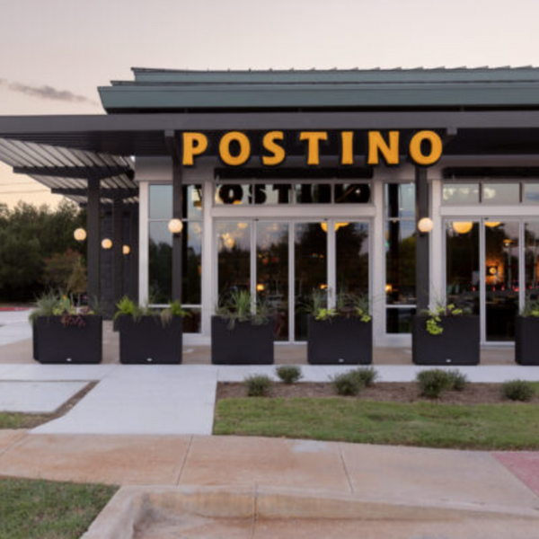 Postino restaurant entrance with large orange sign and planters