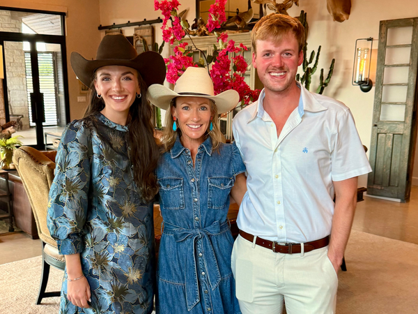 Three smiling adults in cowboy hats pose indoors.