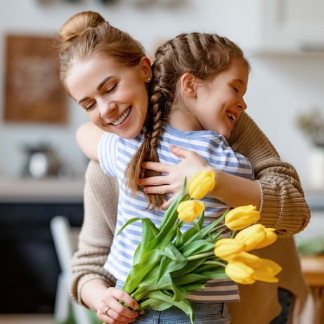 Mother and daughter hugging with yellow flowers.
