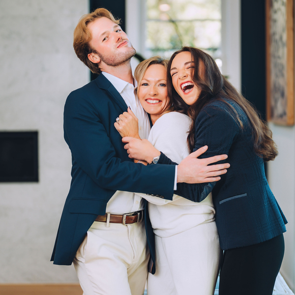 Three people hugging and smiling indoors.