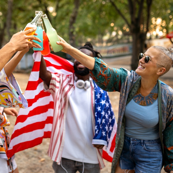 Friends toasting colorful drinks outdoors with American flag