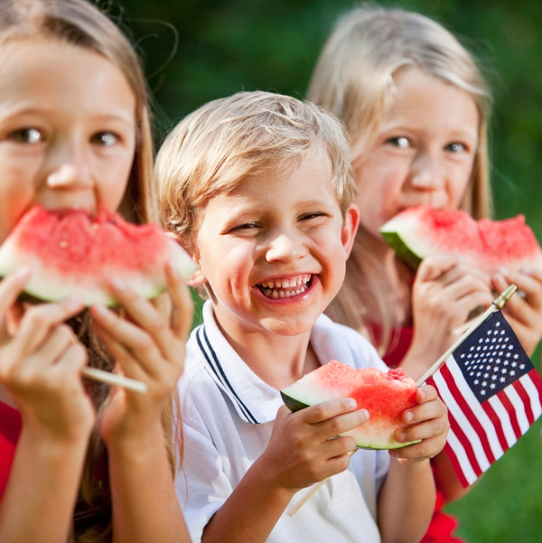 Three children eating watermelon outdoors with small American flag