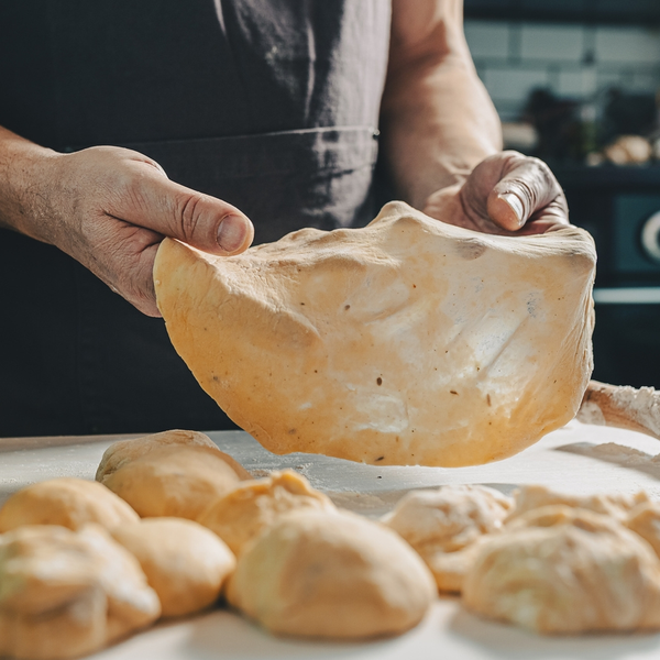 Rope Trix Baker stretching pizza dough over floured work surface
