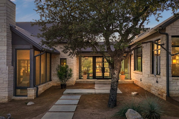 Modern stone courtyard home with tree and illuminated windows