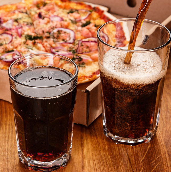 Cola poured beside pizza on wooden table