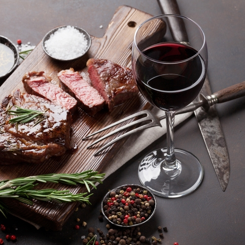 Sliced steak with wine and spices on wooden board.